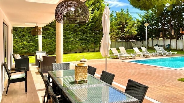 An outdoor patio with a glass-top table and chairs, surrounded by lounge chairs and a swimming pool.