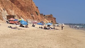 A sandy beach with a rocky cliff and beach umbrellas.