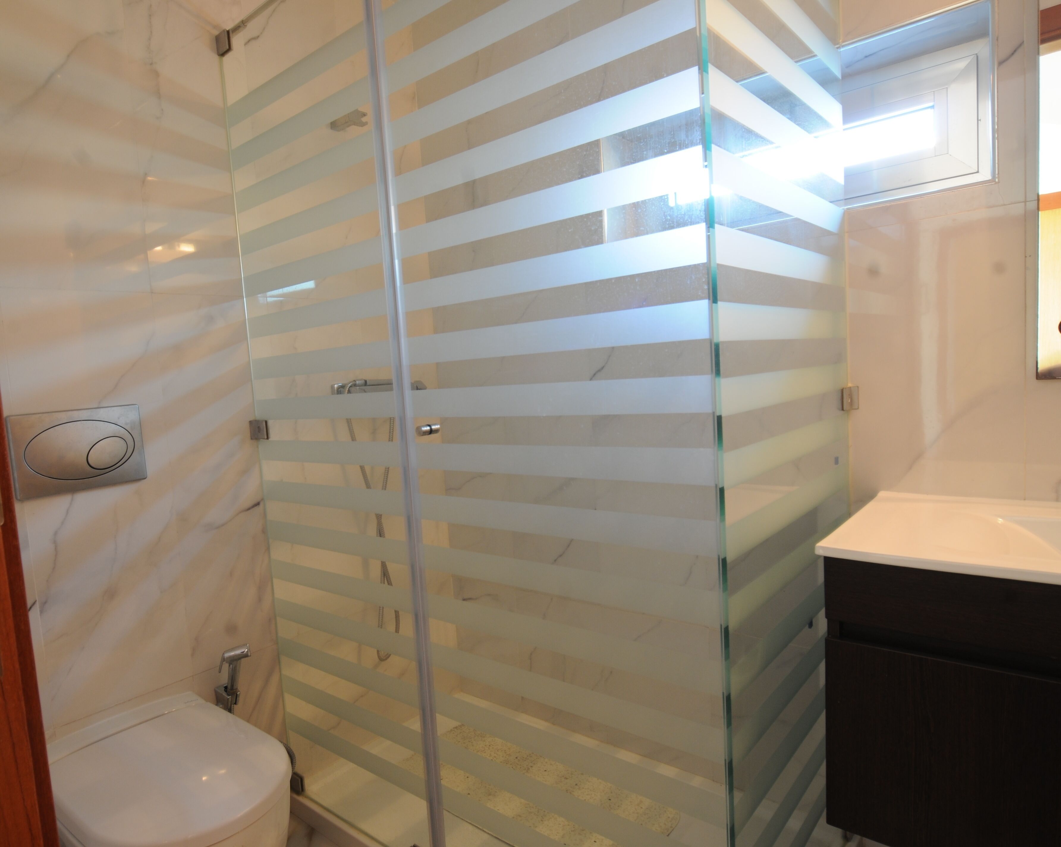A modern bathroom with a glass shower enclosure, a white toilet, and a dark wooden cabinet.