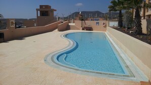 A swimming pool with a curved edge, surrounded by beige walls and a clear blue sky.