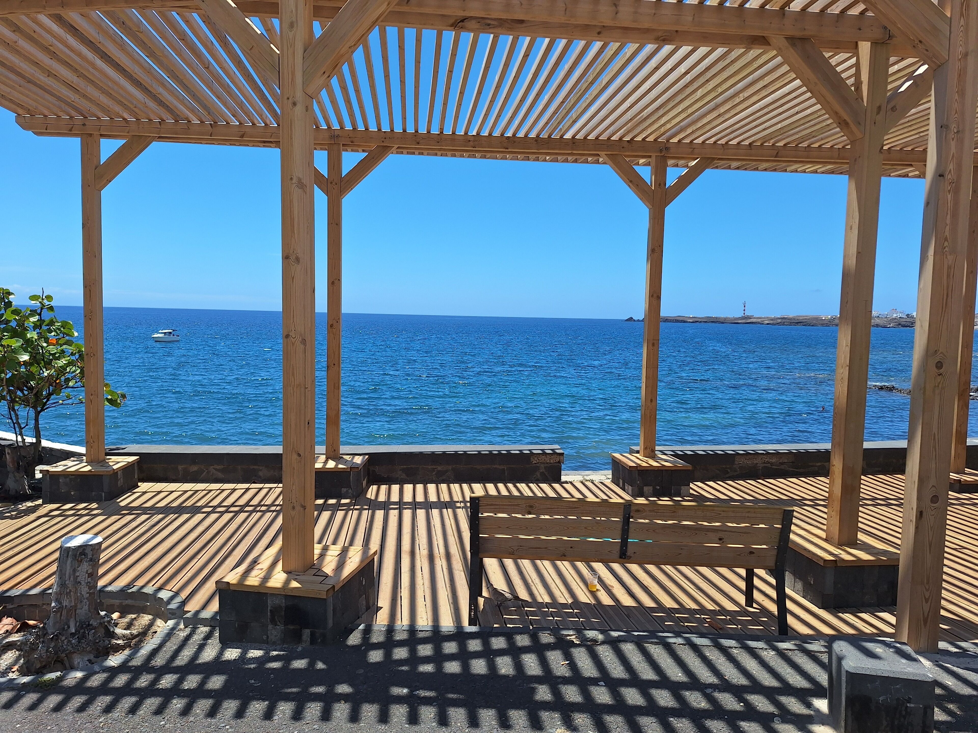 Une terrasse en bois surmontée d’une pergola, offrant une vue sur une mer calme.