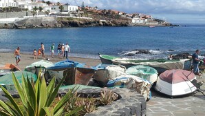 A coastal area with boats on the shore, people walking, and buildings in the background.