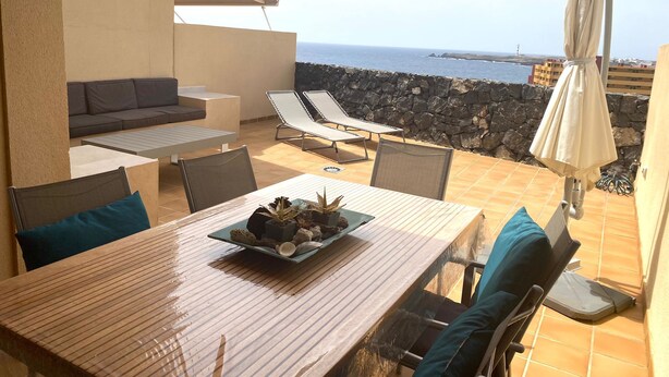 A terrace with a table set for dining, lounge chairs, and a view of the sea.