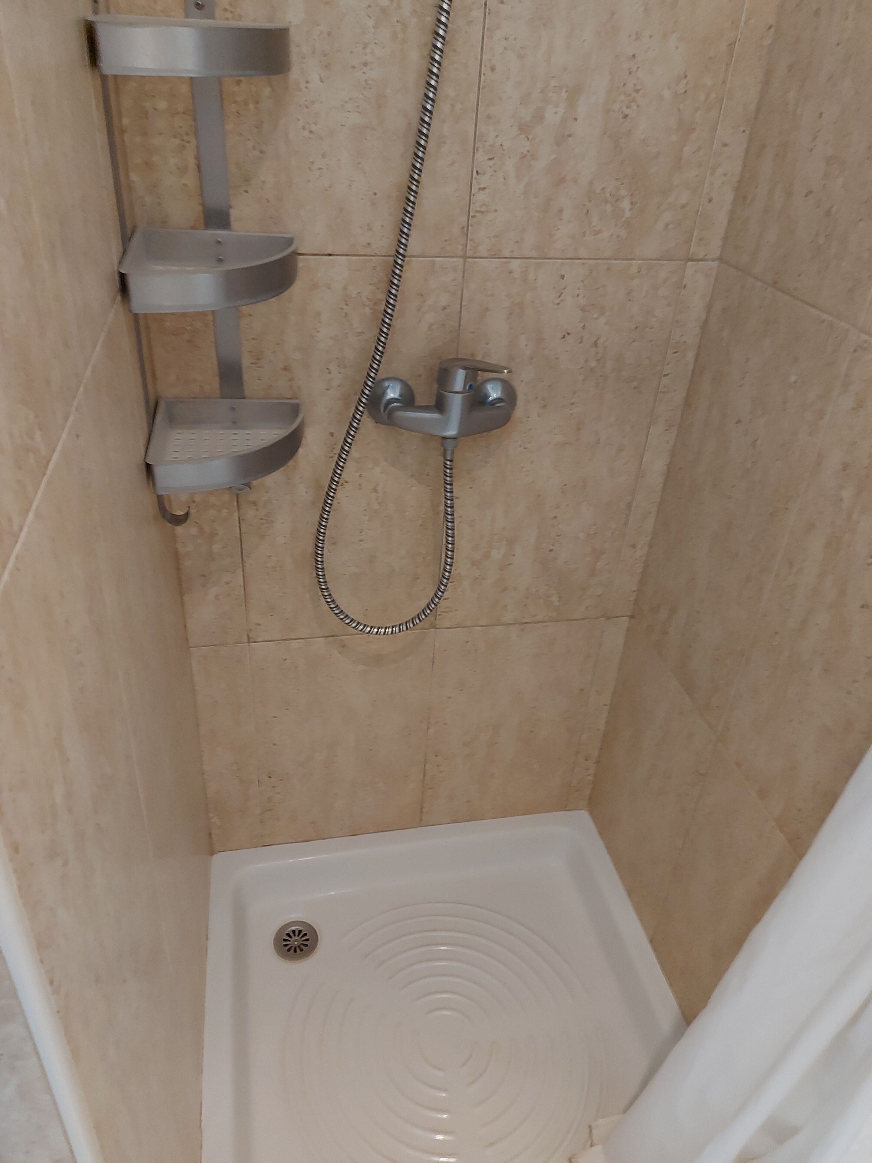 Un espace douche équipé d’un pommeau de douche à main, d’un robinet mural et d’une baignoire blanche.