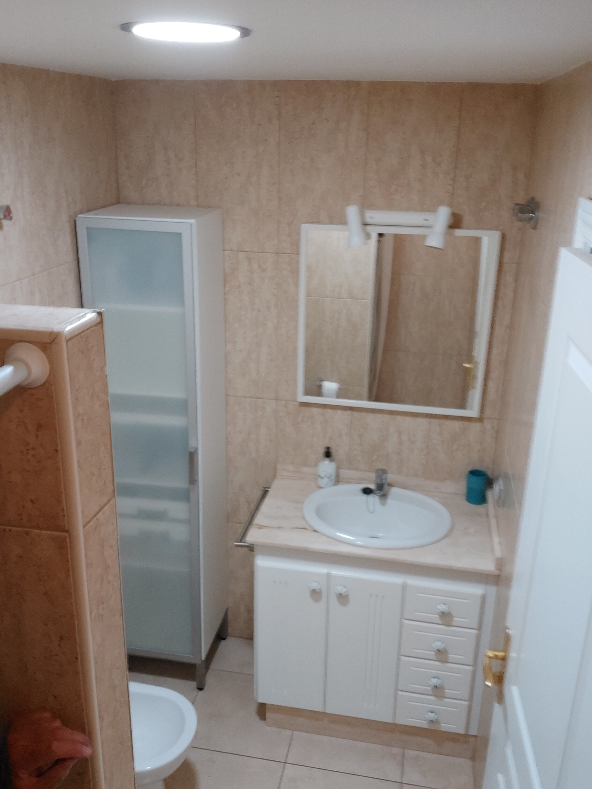 A bathroom with a toilet, sink, cabinet, mirror, and shower.