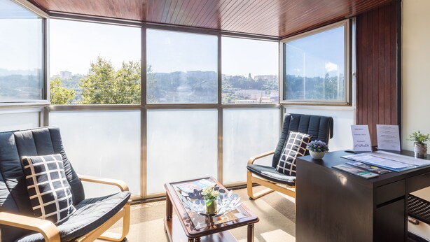 Ein Zimmer mit einem großen Fenster, zwei Stühlen, einem Schreibtisch und einem kleinen Tisch mit einer Vase.