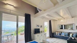 A spacious living area with a large window, a dining table with a bowl, a sofa with decorative pillows, and a television on a cabinet. - Single villa with private pool and lovely sea view (Cava D'aliga)