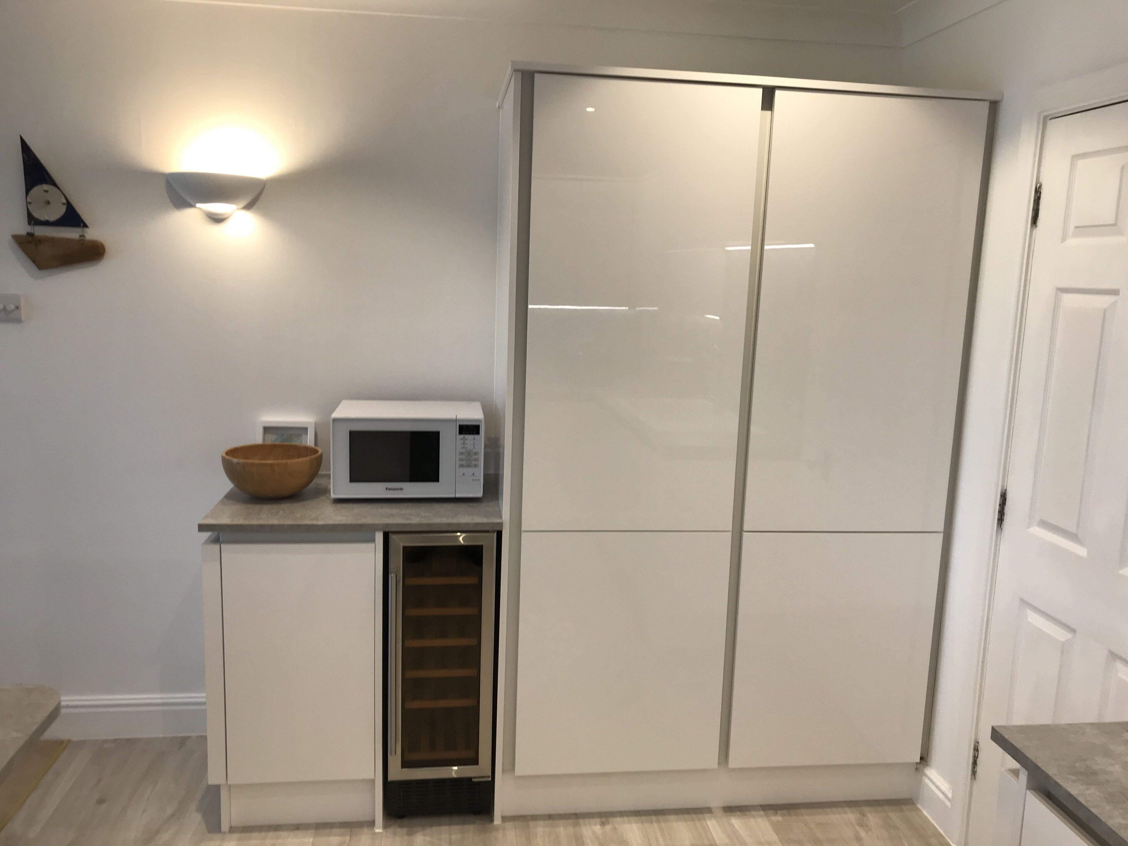 Uma cozinha compacta com micro-ondas embutido, um frigorífico pequeno e uma tigela de madeira sobre a bancada.