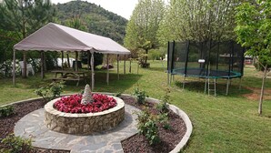 A garden with a stone fountain, a picnic table, a trampoline, and a covered seating area.