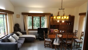 A cozy living room with a sofa, a dining table with chairs, a bookshelf, and a window with curtains.
