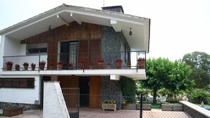 A modern two-story house with a stone facade, a balcony with potted plants, and a gated entrance.