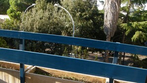 Un balcón con piso estampado, barandal azul y vistas a árboles y edificios al fondo.