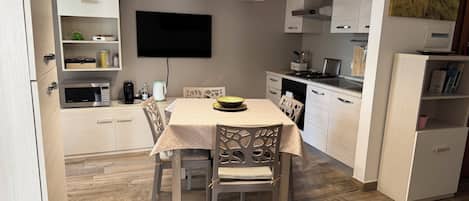 Une cuisine moderne équipée d’une table à manger, de chaises, d’un four à micro-ondes et d’un téléviseur à écran plat fixé au mur.