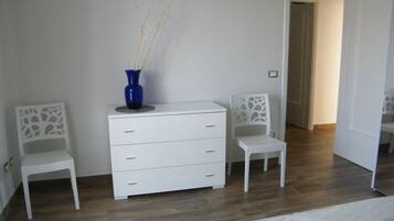 Ein Schlafzimmer mit einem Bett, einer weißen Kommode, zwei Stühlen und einer blauen Vase.