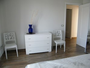 A bedroom with a bed, a white dresser, two chairs, and a blue vase. - Apartment in front of the music conservatory (Lecce)