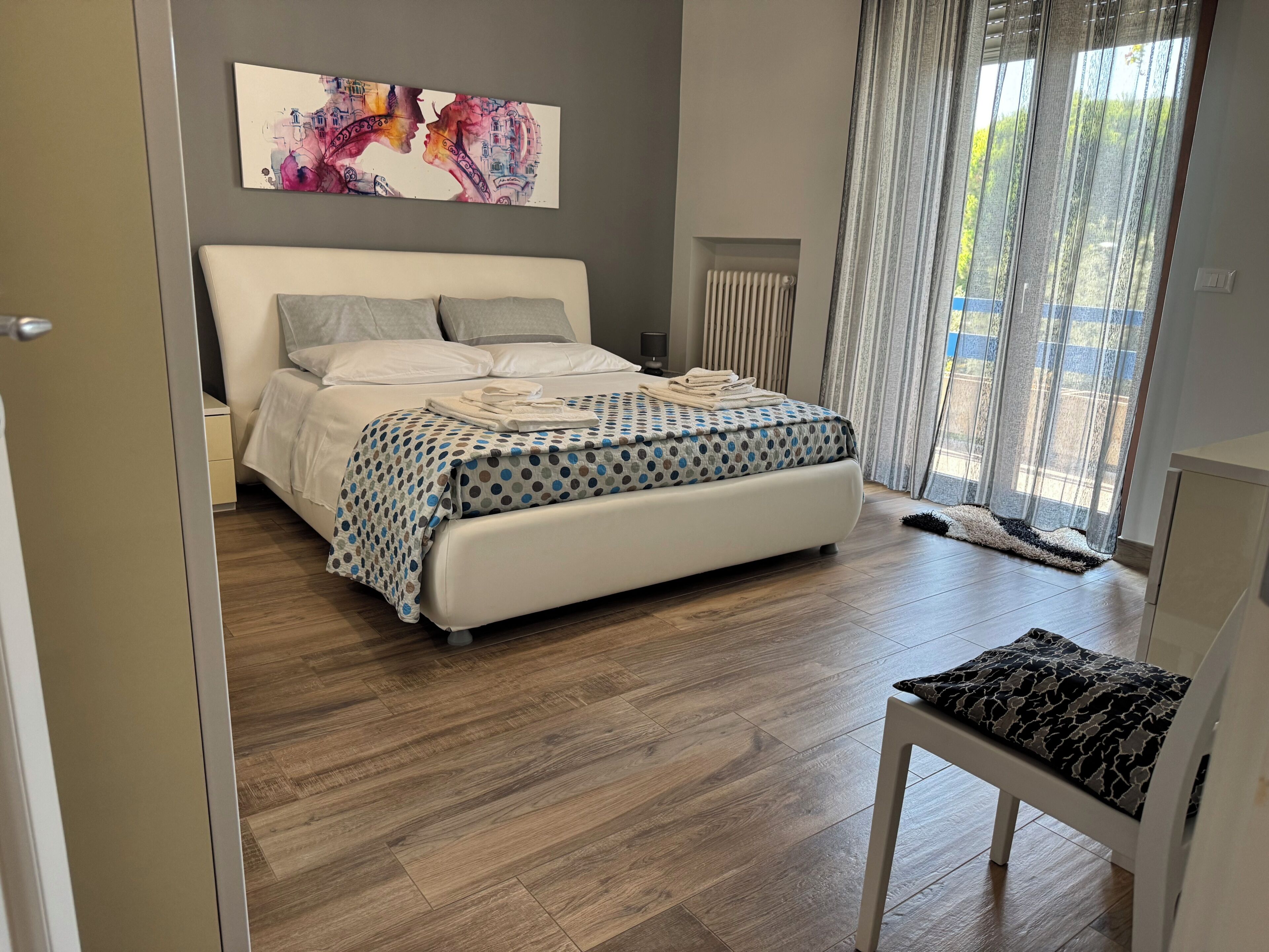 Une chambre moderne avec un grand lit, une table de chevet, un radiateur et une fenêtre avec des rideaux.