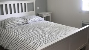 Une chambre à coucher avec un lit, une table de chevet, un luminaire suspendu et une fenêtre.