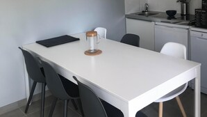 Une table à manger blanche, avec quatre chaises noires, un pichet en verre et un set de table noir.