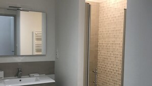 Une salle de bain moderne dotée d’une douche à parois de verre, d’un grand miroir et d’un meuble-lavabo avec un évier et des tiroirs de rangement.
