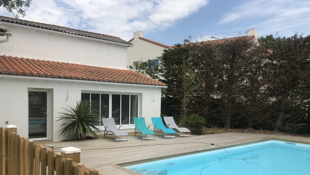 Une piscine dotée d’une terrasse en bois et de chaises longues, entourée d’une clôture en bois et d’arbres.
