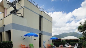A swimming pool with a modern building in the background, a staircase, and outdoor seating with umbrellas. - Luxury Villa with Private Pool, Panoramic Views, Solarium Terrace, BBQ, Parking (Pisa)