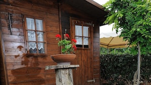 A wooden cabin with a porch, a potted plant, and a garden with pink flowers. - Luxury Villa with Private Pool, Panoramic Views, Solarium Terrace, BBQ, Parking (Pisa)