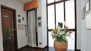A hallway with a wooden door marked "TOILETTE," a potted plant, a large terracotta vase with flowers, and framed pictures on the wall. - Luxury Villa with Private Pool, Panoramic Views, Solarium Terrace, BBQ, Parking (Pisa)