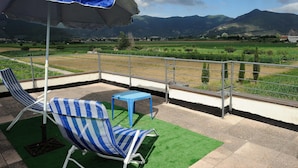 A balcony with two striped lounge chairs, a small table, and a blue umbrella. - Luxury Villa with Private Pool, Panoramic Views, Solarium Terrace, BBQ, Parking (Pisa)