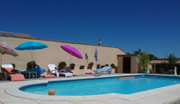 A swimming pool with lounge chairs and umbrellas, a statue, and a building with a tiled roof.
