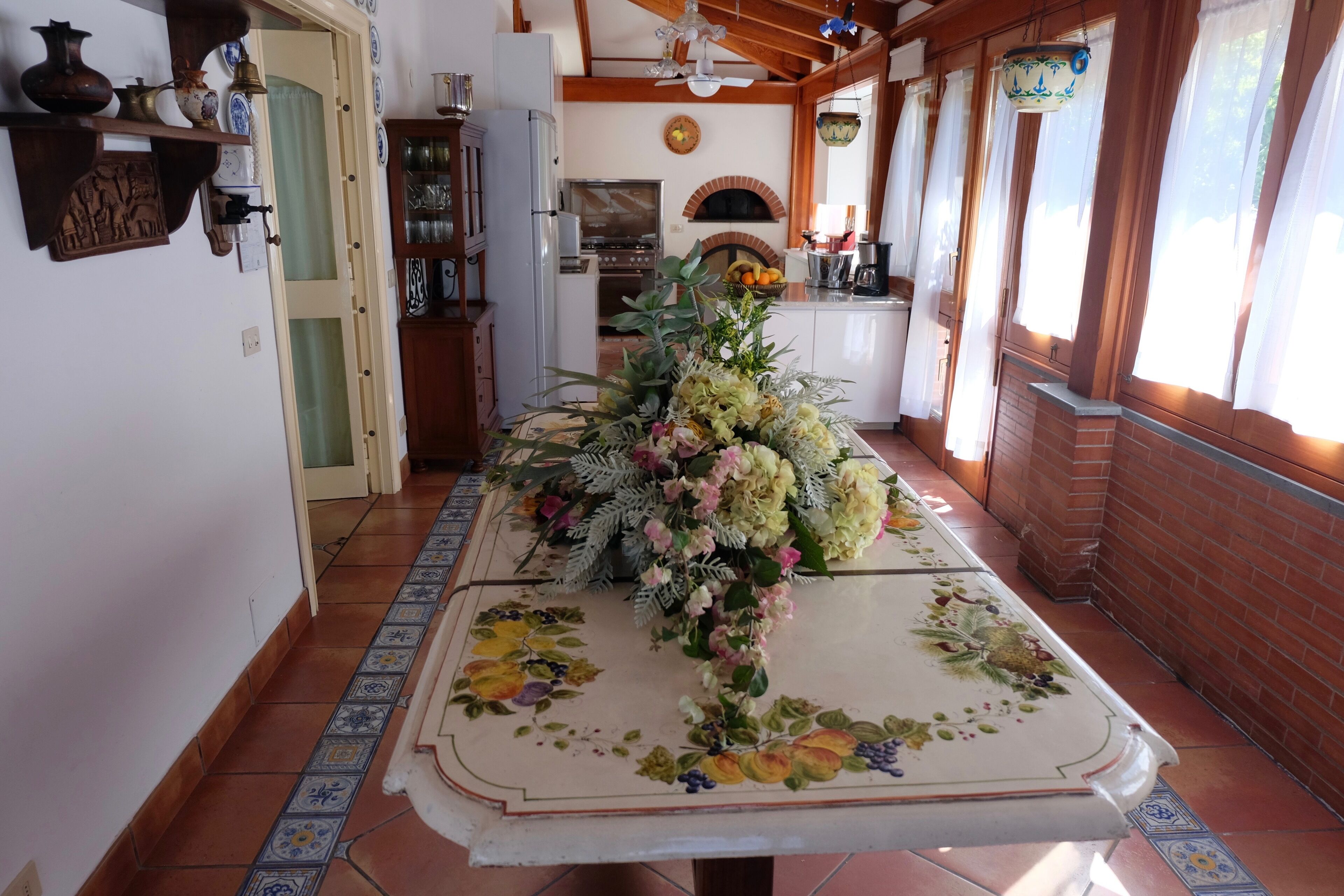 A kitchen with a central island, a brick oven, and a dining area with a floral tablecloth.