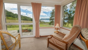 A room with a large window, a bed, a chair, and a small table.