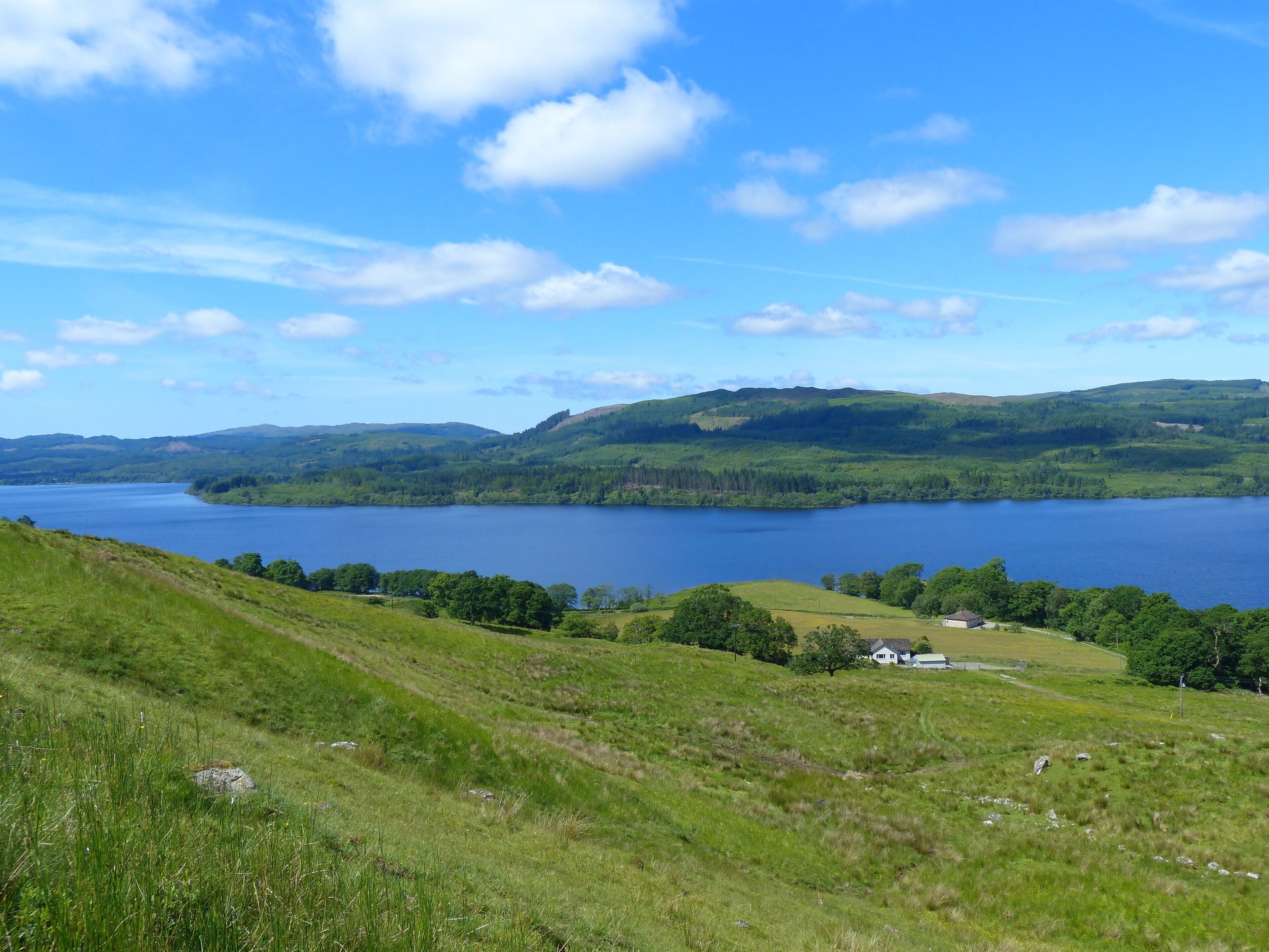 A scenic view of a lake surrounded by green hills and a small house in the foreground.