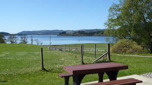 A picnic table in a grassy area with a view of a lake and hills in the background.