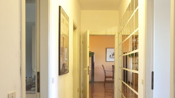 A hallway with wooden flooring, white walls, and a door with a glass panel on the right.