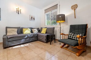 A living room with a grey sectional sofa, a wooden armchair, a floor lamp, and a small table.