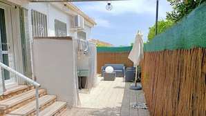 Eine Terrasse mit einer Steintreppe zu einer Tür, einem überdachten Sitzbereich mit einem runden Tisch und einem Bambuszaun.