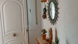 Ein Zimmer mit einer weißen Tür, einem Spiegel mit dekorativem Rahmen und mehreren Blumentöpfen auf einem Holzregal.