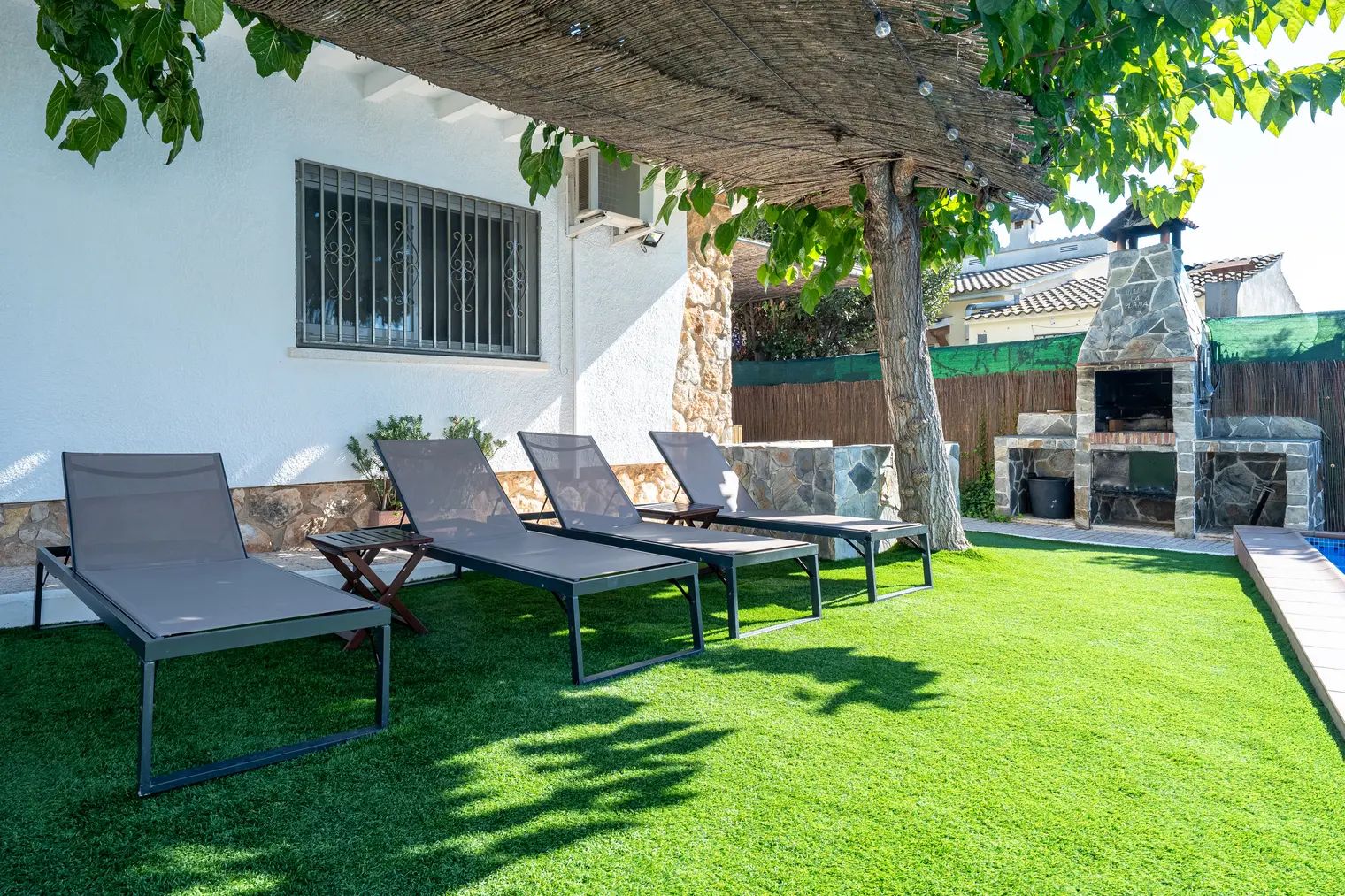 Un jardin avec quatre chaises longues, un espace barbecue en pierre et une petite piscine.