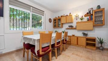 A dining area with a table set for four, wooden chairs, a kitchen area with cabinets and a countertop, and a window with a view of greenery.