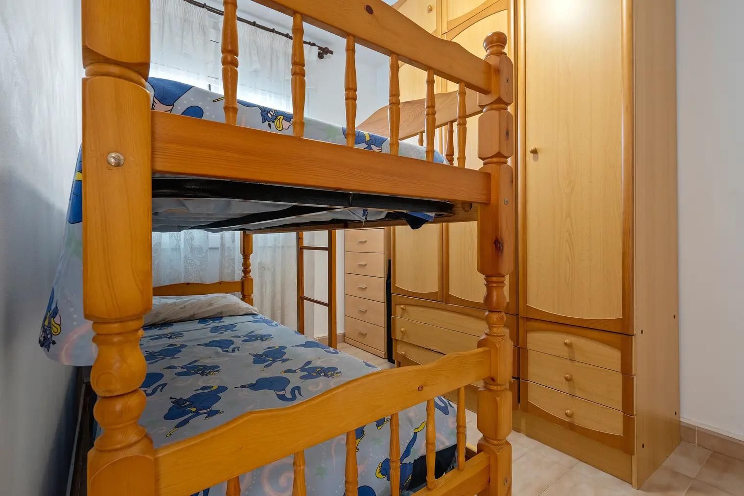 A bunk bed with a lower bunk, a wooden wardrobe with multiple drawers, and a window with curtains.