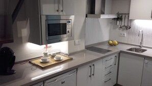 A modern kitchen with white cabinetry, a built-in microwave, a kettle, and a tray with cups and a teapot. - Interior design and exclusive design (Sevilla)