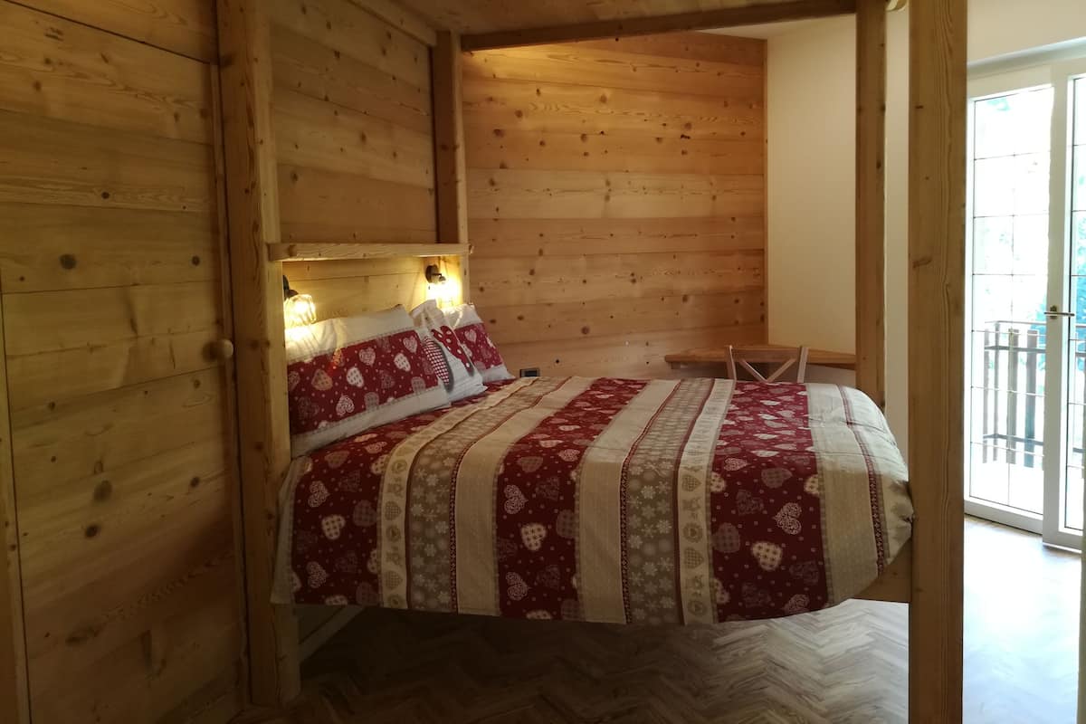A wooden cabin-style room with a bed, two bedside lamps, and a window with a view.