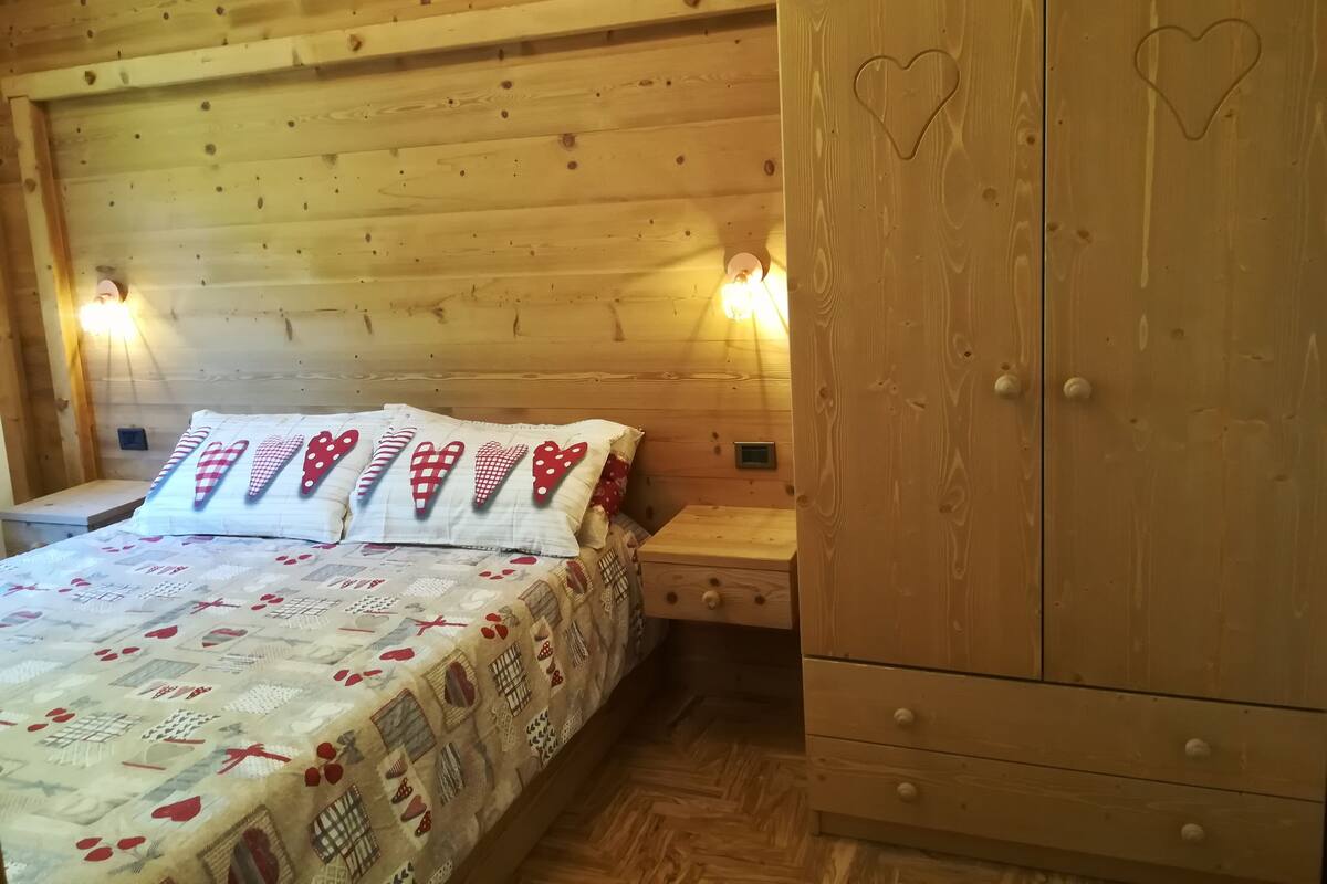 A wooden cabin bedroom with a bed, nightstands, and a wardrobe.