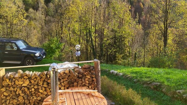 En träbeklädd bastu med utsikt över bergen, en parkerad bil och en hög med ved.