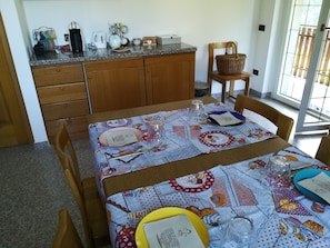 A dining area with a table set for two, featuring a patterned tablecloth, various dishes, and a coffee maker on the counter. - Romantiche Orobie B&B (Roncobello)