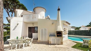 A villa with a stone patio, outdoor seating, a pool, and a chimney.