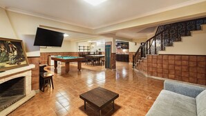 A spacious living area with a pool table, a flat-screen TV, a fireplace, and a staircase with decorative railings.