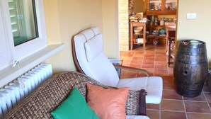 Ein gemütliches Wohnzimmer mit einer Couch, Sesseln, einem großen Holzbottich und einer Küchenzeile im Hintergrund.