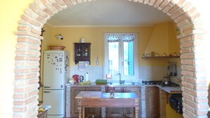 Eine Küche mit einer Ziegelbogenarchitektur, einem Kühlschrank, einem Holztisch und einem Fenster mit Fensterläden.