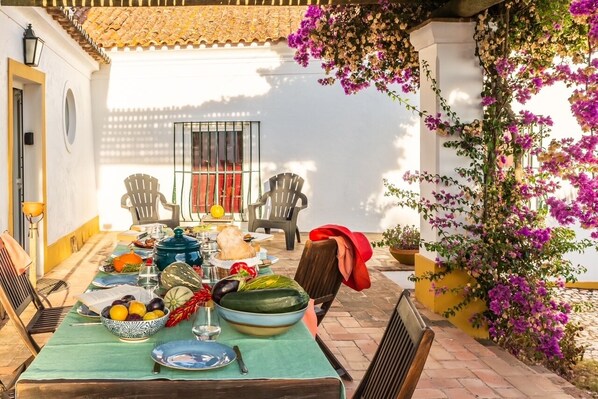 An outdoor dining area with a table set for a meal, surrounded by chairs and a decorative plant.